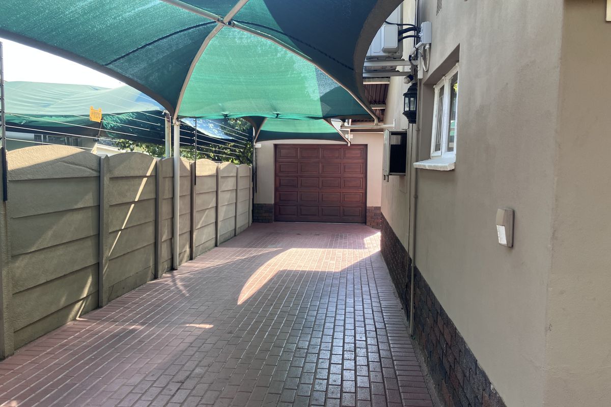 A paved side driveway featuring a green shade sail, precast concrete boundary wall, and access to a garage.