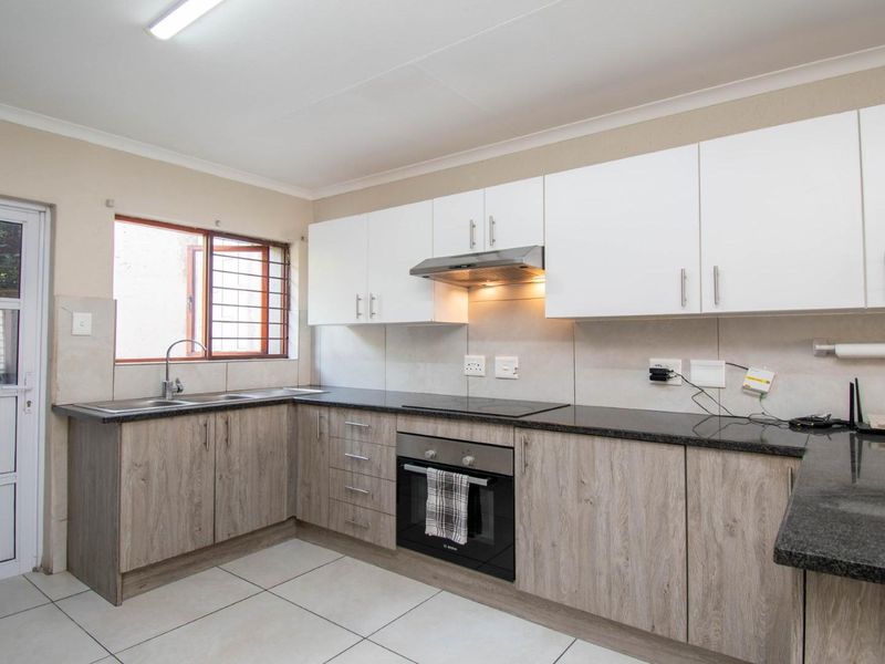 A clean, modern kitchen featuring white upper cabinets, wood-grain lower cabinetry, granite countertops, and integrated appliances including an oven and extractor fan.