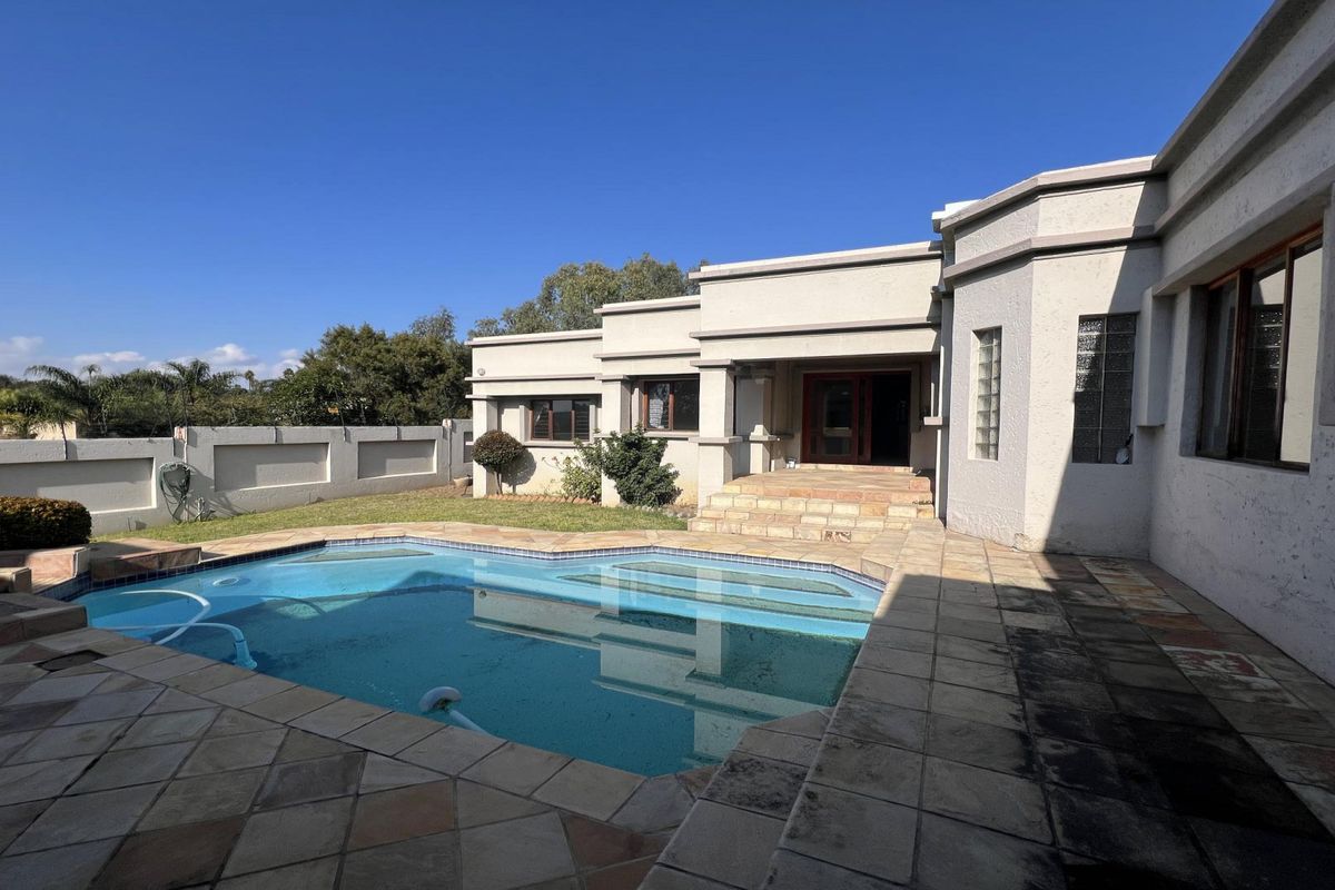 Rear exterior view featuring a swimming pool, stone paved patio area, and boundary wall, providing a private outdoor entertainment space.
