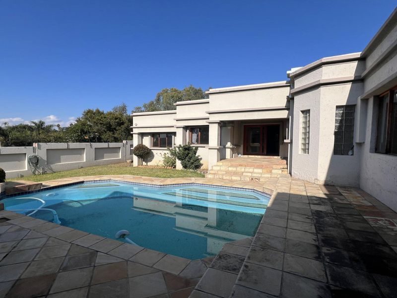 Rear exterior view featuring a swimming pool, stone paved patio area, and boundary wall, providing a private outdoor entertainment space.