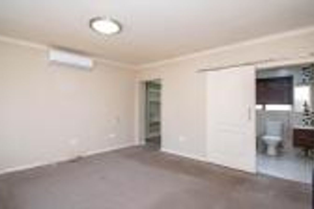 Spacious bedroom featuring neutral walls, carpet flooring, an air conditioning unit, and an en-suite bathroom accessible via a sliding door.