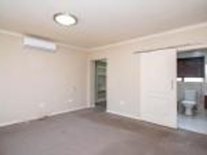 Spacious bedroom featuring neutral walls, carpet flooring, an air conditioning unit, and an en-suite bathroom accessible via a sliding door.