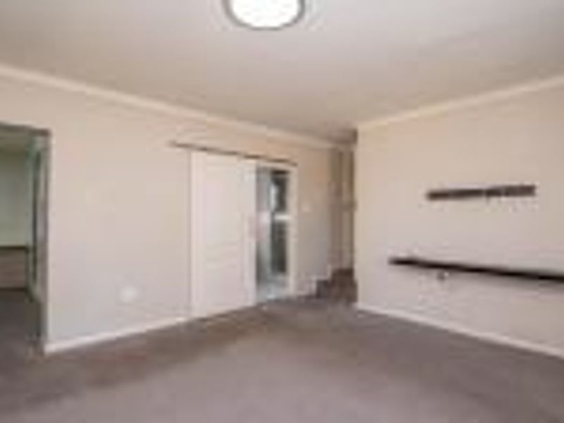 A spacious, empty living room featuring neutral walls, carpeted flooring, a sliding door, and a built-in floating shelf.