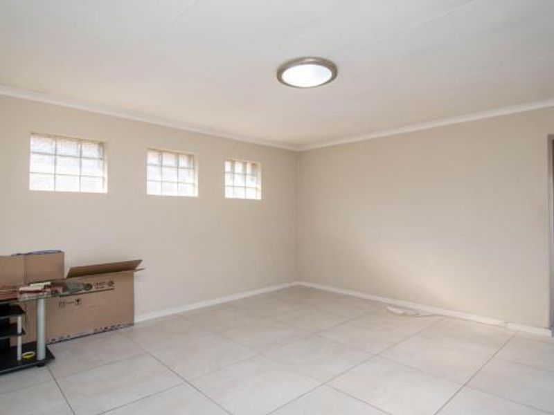 A spacious, empty living area featuring neutral walls, tiled flooring, and multiple glass block windows providing natural light.