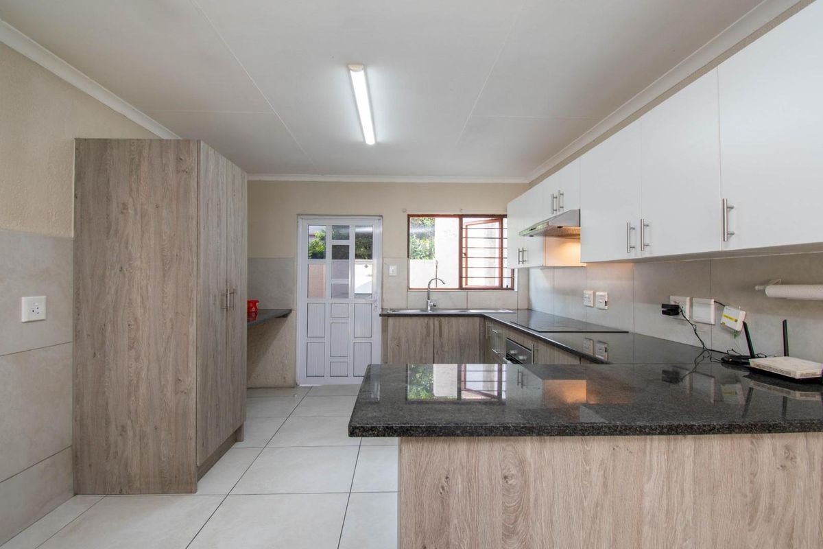 Modern kitchen featuring granite countertops, ample built-in cabinetry, tiled flooring, and an integrated extractor fan, offering a clean and functional workspace.