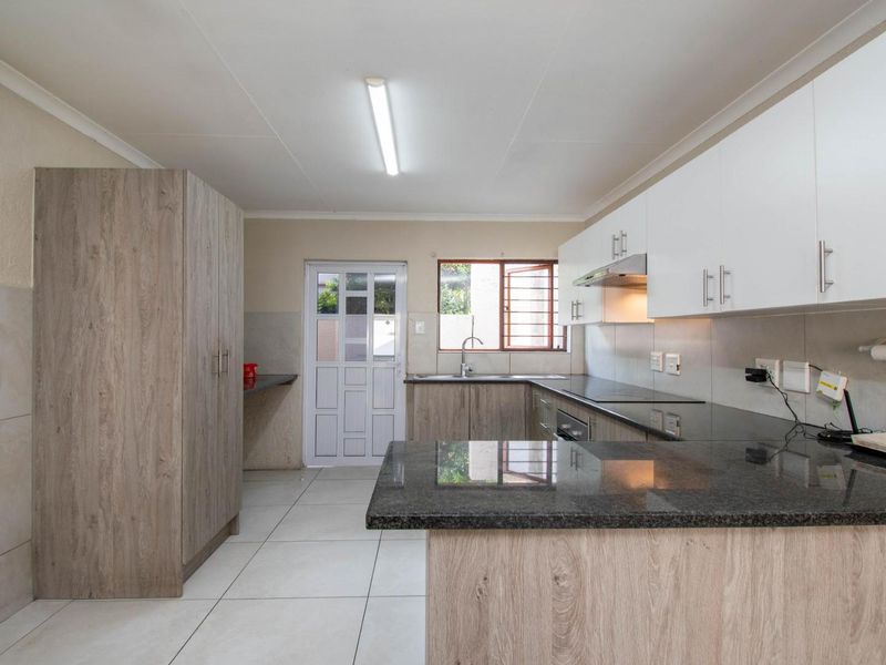 Modern kitchen featuring granite countertops, ample built-in cabinetry, tiled flooring, and an integrated extractor fan, offering a clean and functional workspace.