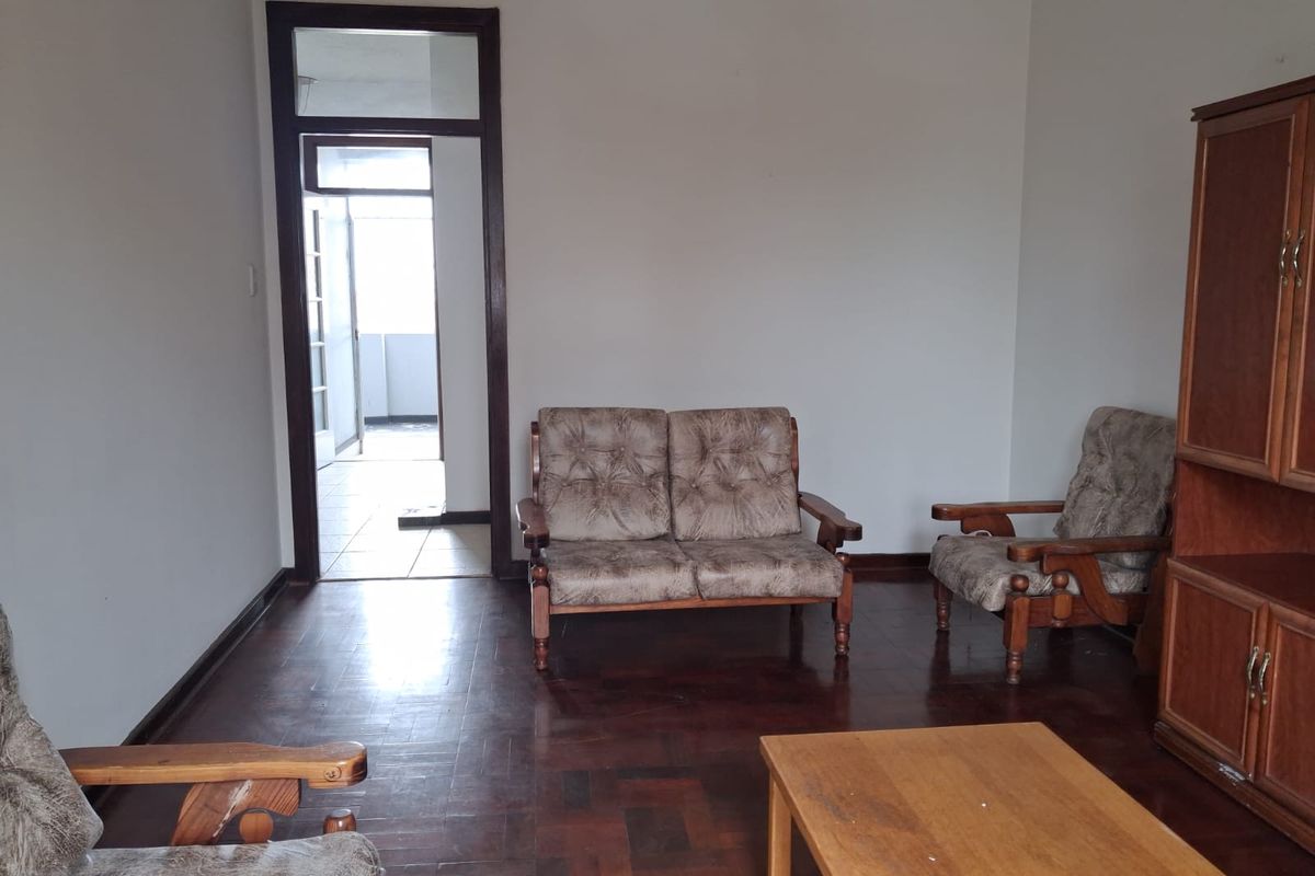 A living room featuring traditional parquet flooring and a timber door frame leading to an adjacent balcony area.
