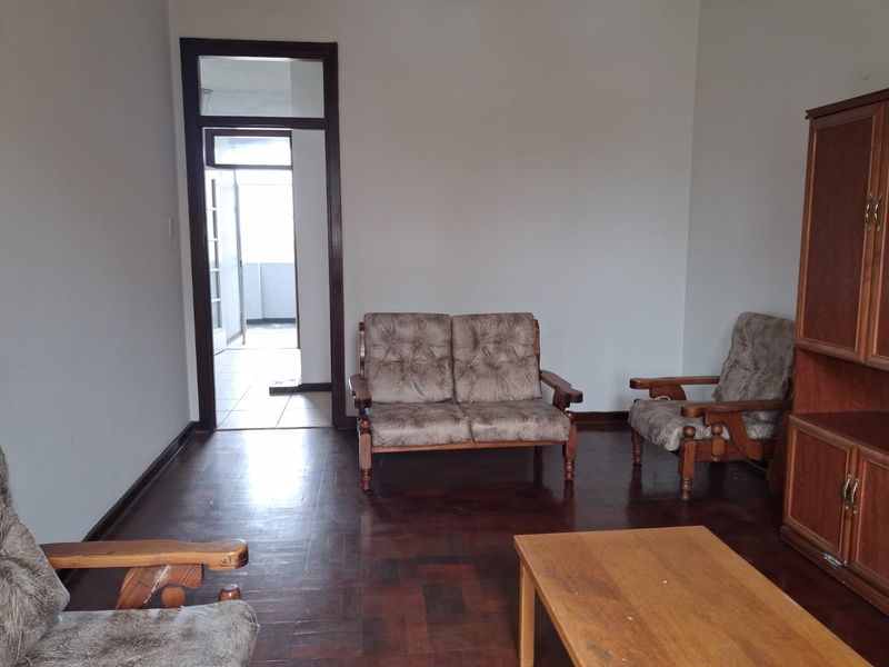 A living room featuring traditional parquet flooring and a timber door frame leading to an adjacent balcony area.