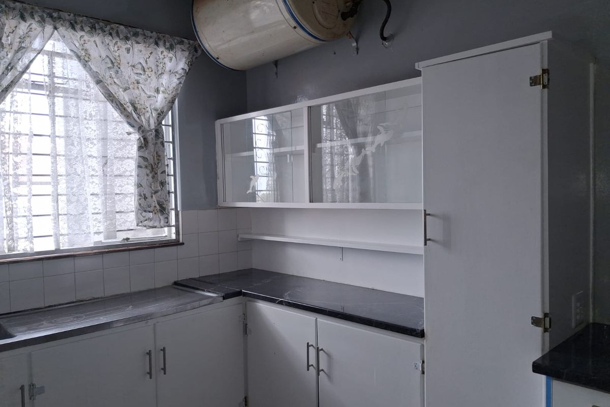 A functional kitchen area featuring white built-in cabinetry, dark laminate countertops, tiled splashbacks, and an overhead electric water heater.
