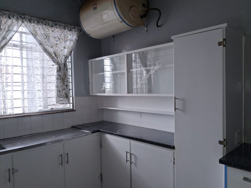 A functional kitchen area featuring white built-in cabinetry, dark laminate countertops, tiled splashbacks, and an overhead electric water heater.