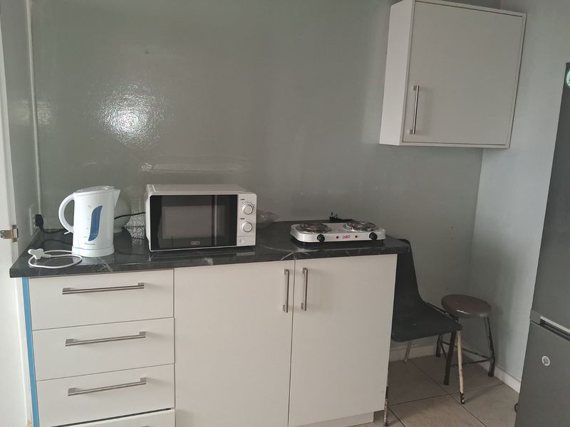 A compact kitchen area featuring white built-in cabinetry, a dark laminate countertop, and a wall-mounted storage cupboard.