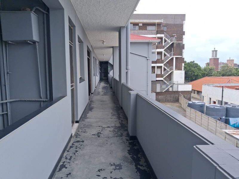 An exterior apartment building walkway featuring a concrete floor with visible wear and metal security gates providing access to units.