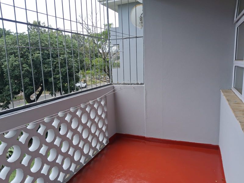 A clean, covered balcony featuring a painted floor, decorative breeze block screen, and security bars, offering a functional outdoor space.