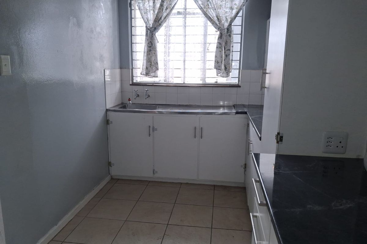 A functional kitchen space featuring built-in cabinetry, a stainless steel sink, tiled splashbacks, and tiled flooring, ready for modernization.