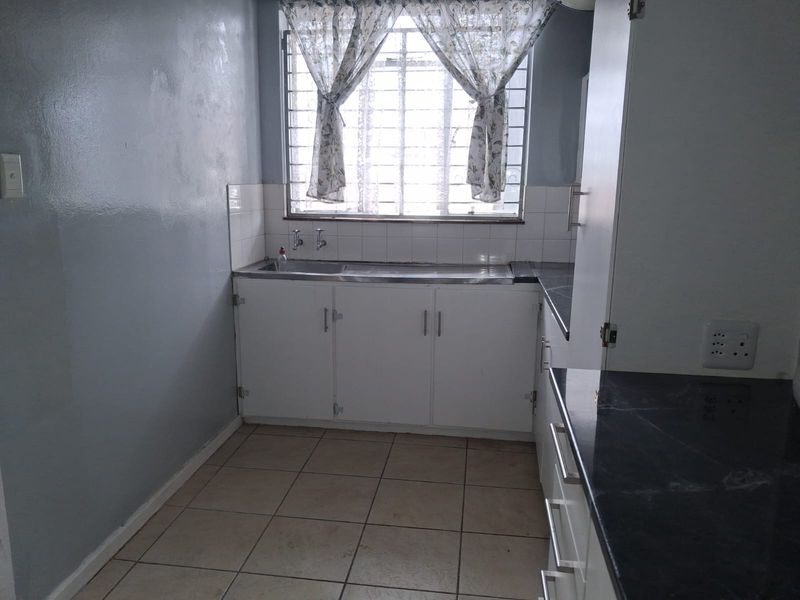 A functional kitchen space featuring built-in cabinetry, a stainless steel sink, tiled splashbacks, and tiled flooring, ready for modernization.