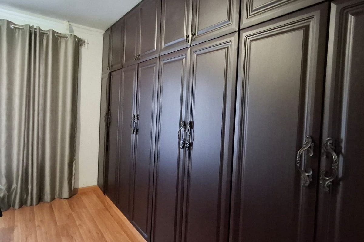A bedroom featuring extensive dark wood built-in cupboards and laminate flooring, providing ample storage space.