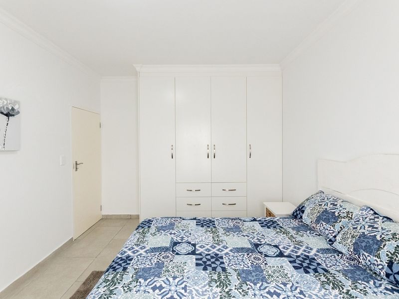 A clean and bright bedroom featuring neutral tiled flooring, white built-in cupboards with ample storage, and classic ceiling cornicing.