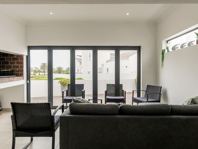 A covered patio area featuring a built-in braai, modern tiled flooring, and large aluminium stacker doors providing seamless access to the outdoor space.