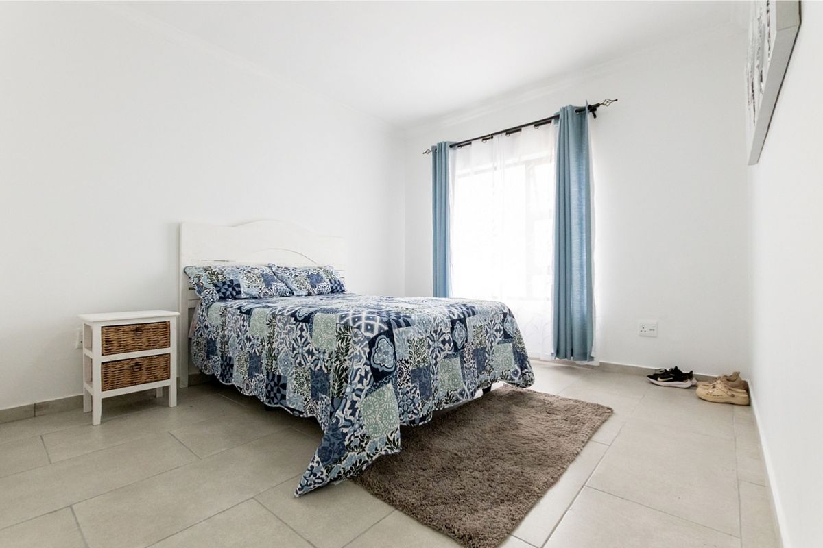 A bright and neutral bedroom featuring tiled flooring and a window with installed curtain rods.