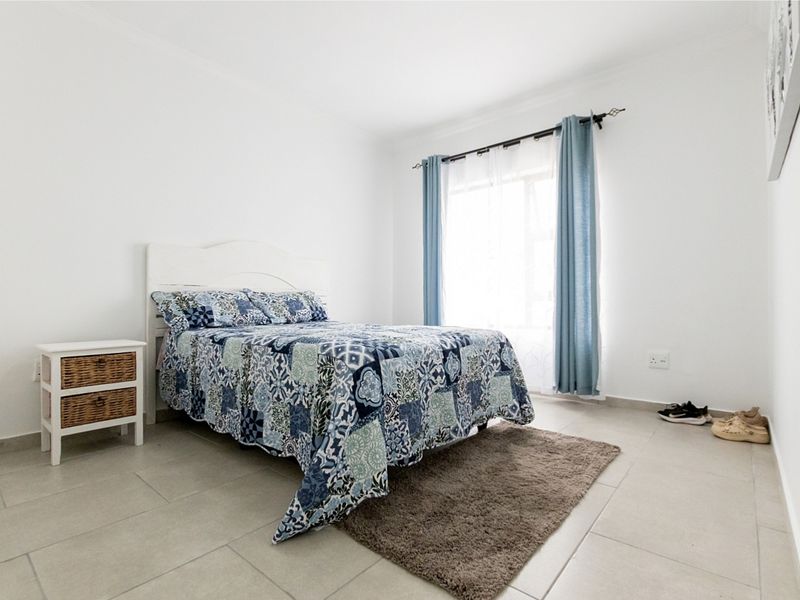 A bright and neutral bedroom featuring tiled flooring and a window with installed curtain rods.