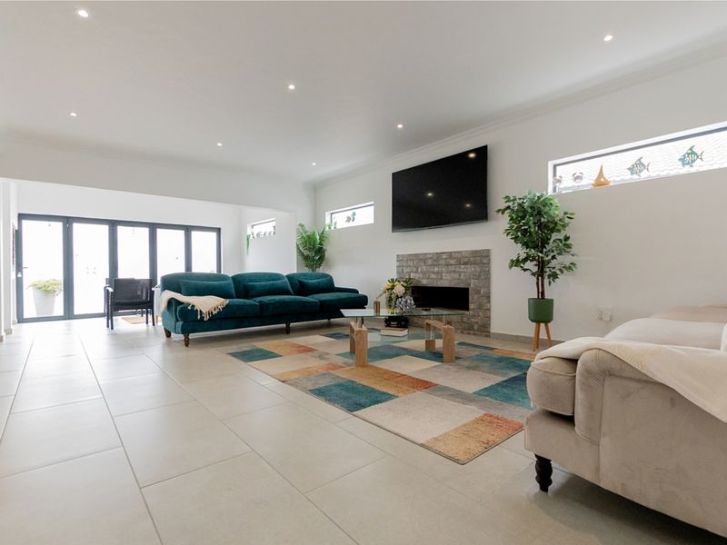 Spacious living room featuring a stone-clad fireplace, modern tiled flooring, recessed lighting, and large bi-fold doors providing seamless access to the outdoor area.