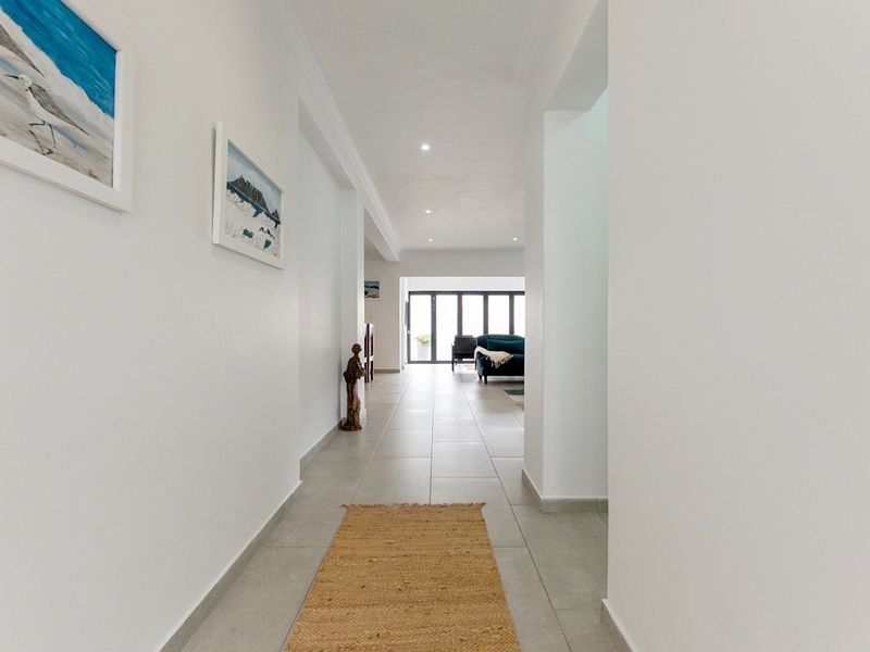 A bright, neutral hallway featuring tiled flooring and recessed downlighting, providing a clean transition between living spaces.