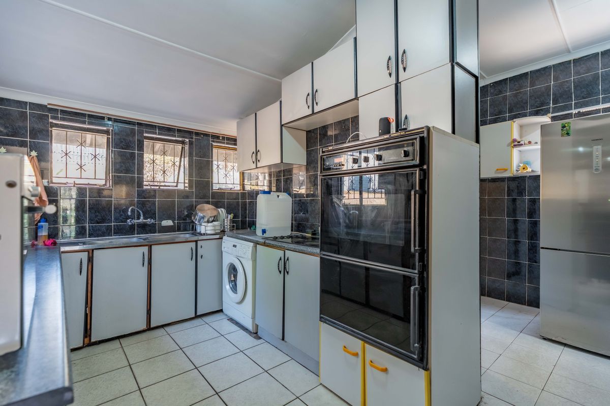 Functional kitchen featuring built-in cabinetry, a double wall oven, hob, tiled backsplash, and tiled flooring with security bars on the windows.