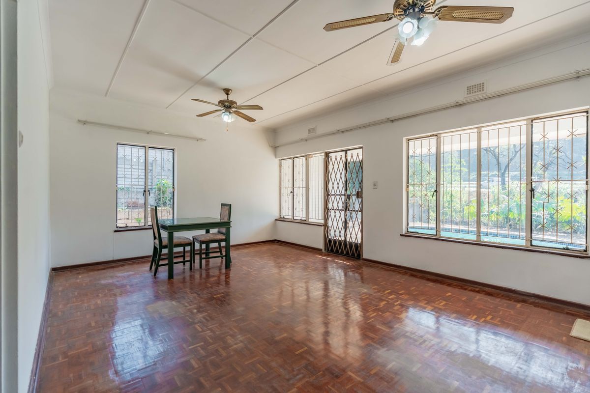 Spacious living area featuring polished parquet flooring, dual ceiling fans, and large windows with security bars overlooking the garden and pool area.