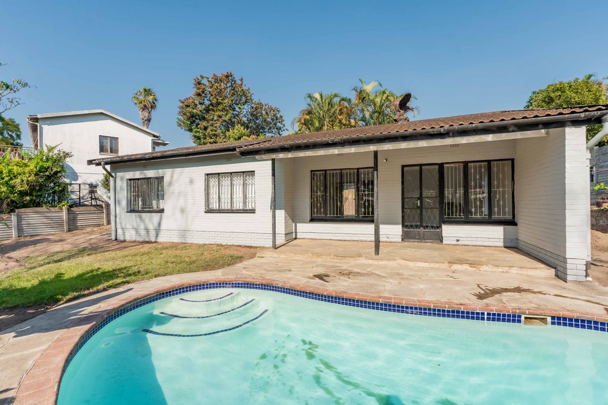 Rear exterior view featuring a swimming pool, paved patio area, and a single-story brick home with security bars on windows.
