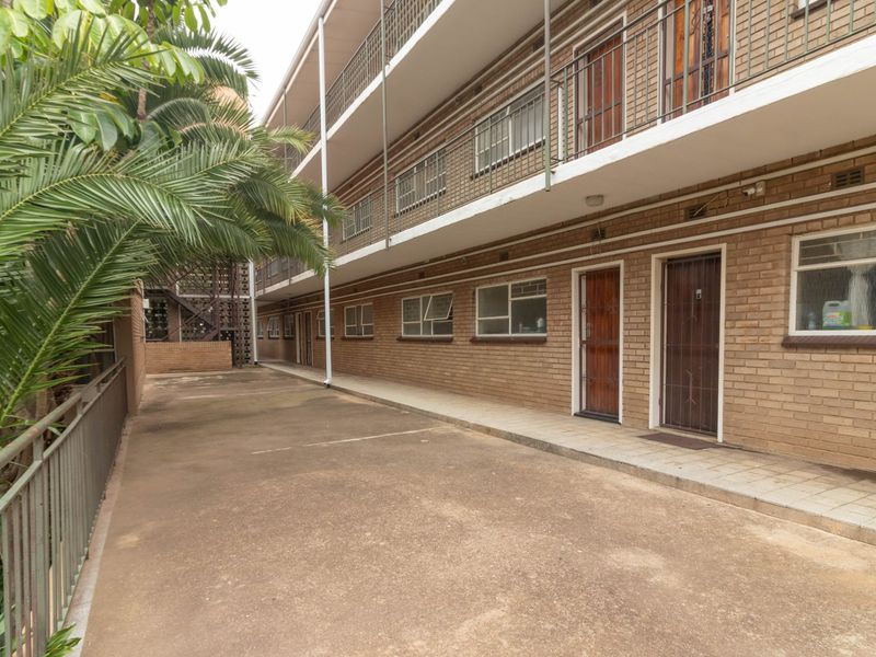 Exterior view of a multi-story apartment building featuring face brick facade, metal security gates, and concrete walkways.