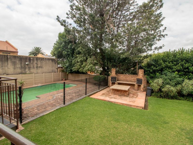 Rear garden featuring a swimming pool with safety fencing, a paved patio area, and a brick built-in braai facility.