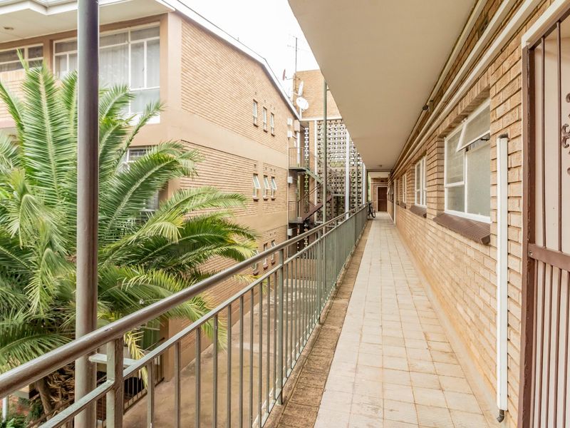 An exterior walkway or balcony featuring tiled flooring, a metal balustrade, and brick building facade in an apartment complex setting.
