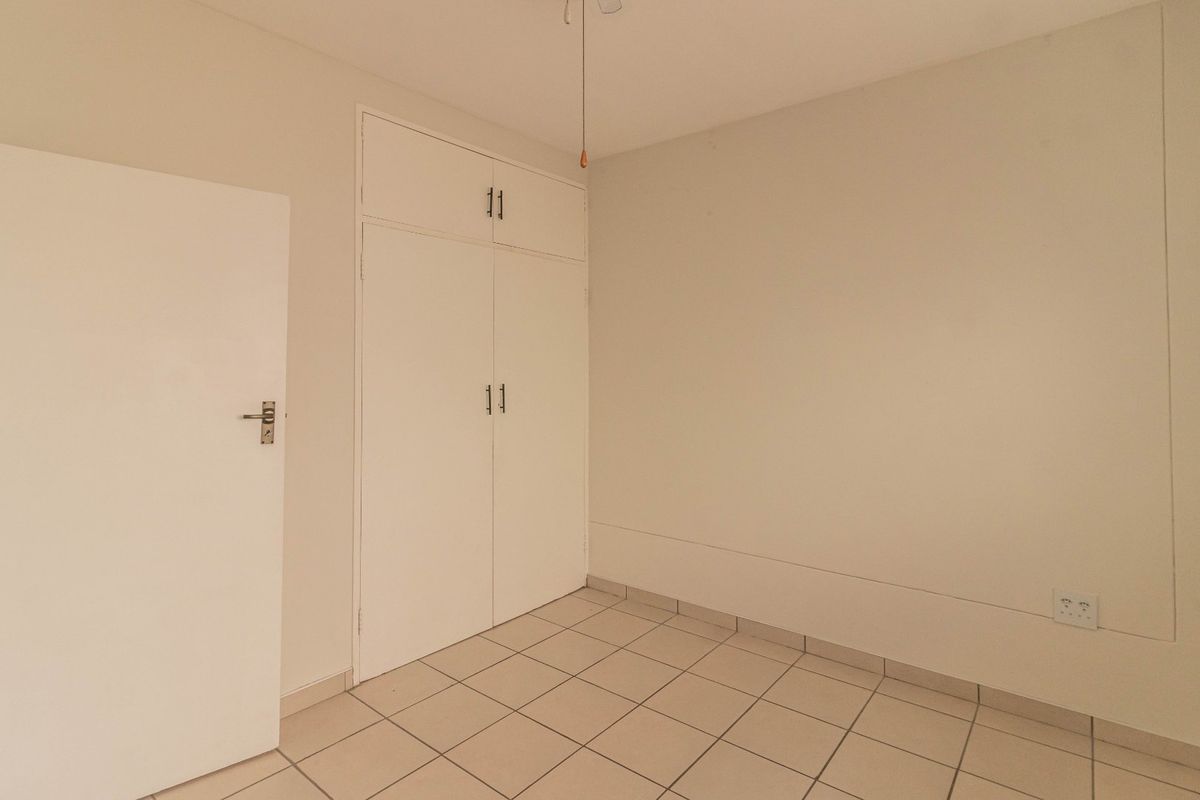 An empty bedroom featuring neutral walls, tiled flooring, and built-in storage cupboards.