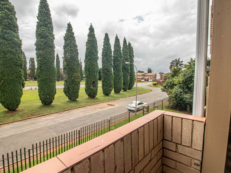 A private balcony featuring a brick balustrade with tiled coping, overlooking a quiet residential street with mature cypress trees.