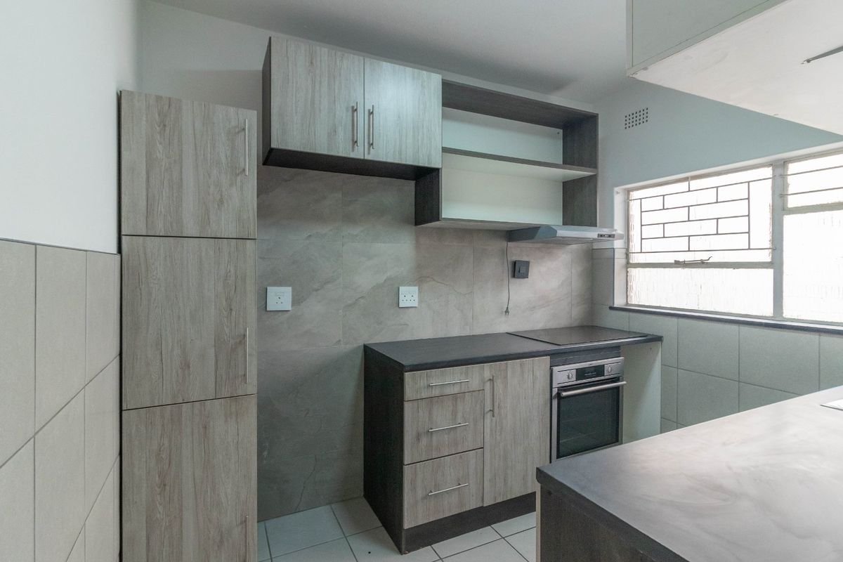 A modern, well-maintained kitchen featuring wood-grain cabinetry, stone-look countertops, built-in oven and hob, and tiled finishes throughout.