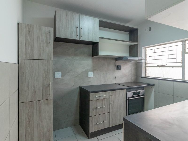 A modern, well-maintained kitchen featuring wood-grain cabinetry, stone-look countertops, built-in oven and hob, and tiled finishes throughout.