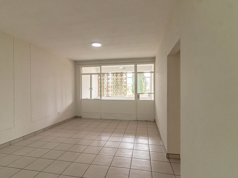 A bright, empty living room featuring neutral tiled flooring and a large glass door providing natural light and access to the exterior.