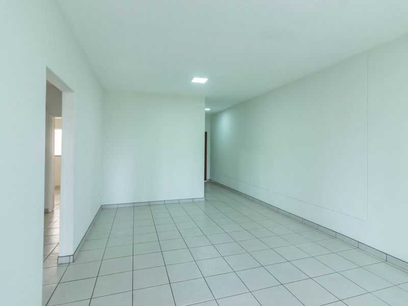 A bright, empty living area featuring neutral ceramic floor tiles and recessed ceiling lighting, offering a clean and versatile space.