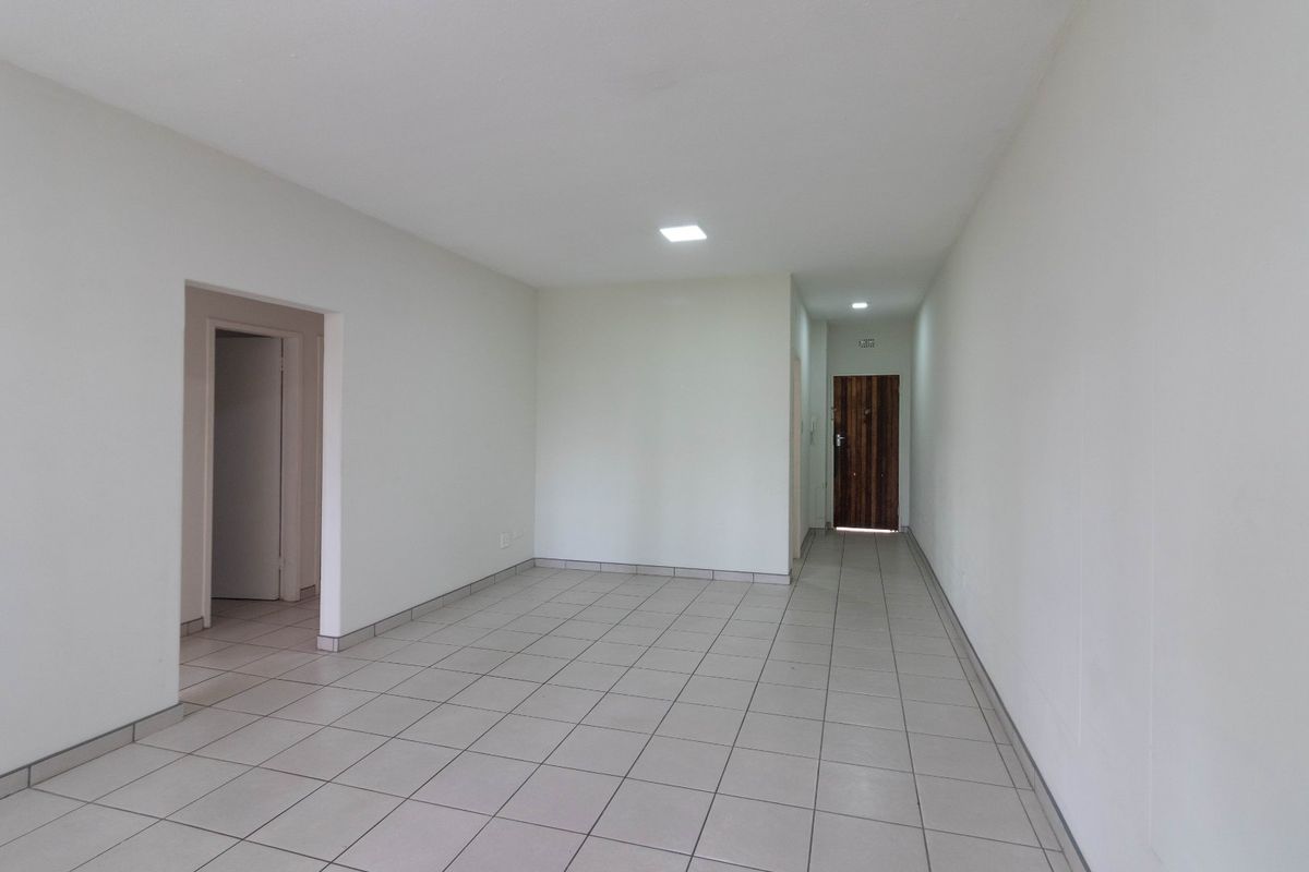 A bright, open-plan living area featuring neutral tiled flooring, recessed downlighting, and a secure timber entrance door.