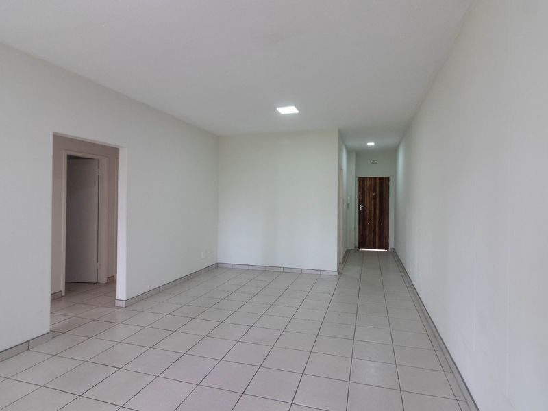 A bright, open-plan living area featuring neutral tiled flooring, recessed downlighting, and a secure timber entrance door.