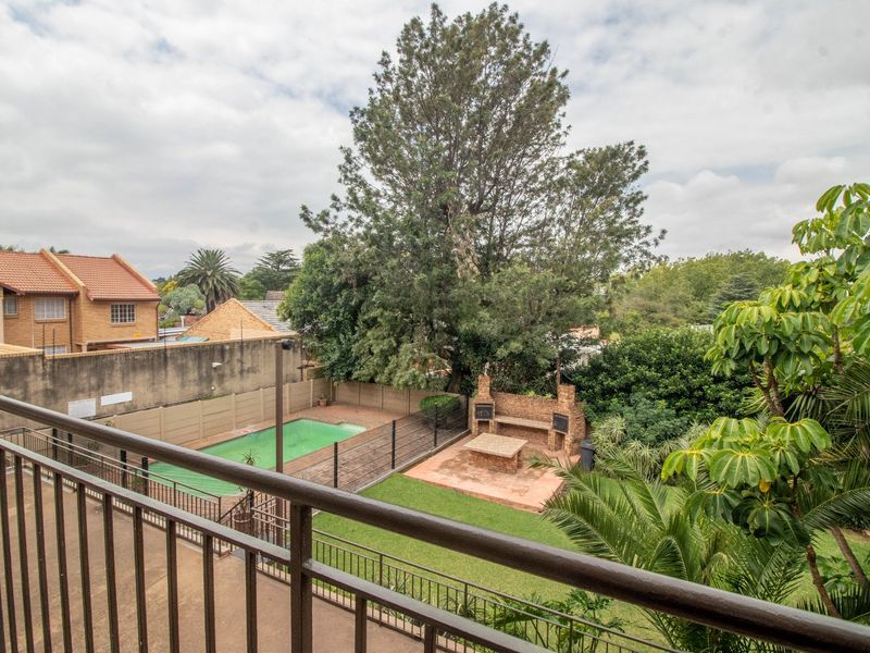 Elevated view of a communal garden area featuring a swimming pool, lawn, and a built-in brick braai facility.