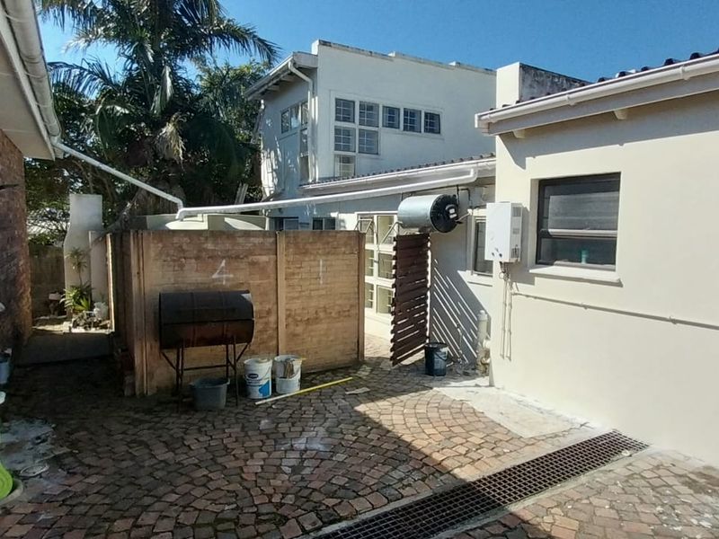 Rear exterior courtyard area featuring brick paving, drainage channels, and external utility fixtures including a gas geyser and guttering system.