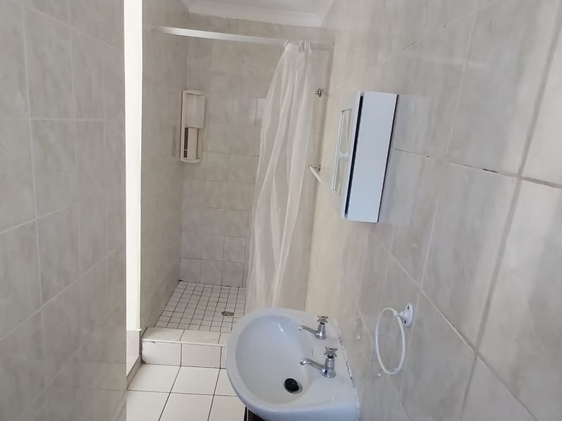 A functional bathroom featuring a wall-mounted basin and a tiled shower area with a curtain rail, presenting a dated but clean aesthetic.