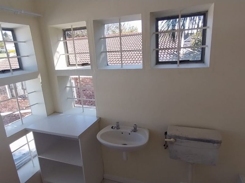 A functional bathroom space featuring a wall-mounted basin, toilet cistern, and built-in shelving, with security bars installed on the windows.