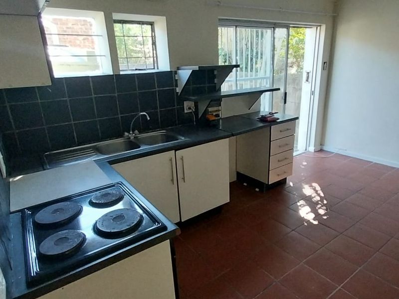 A functional kitchen featuring built-in cabinetry, an electric hob, and tiled splashbacks, with direct access to the outdoor area via a sliding glass door.