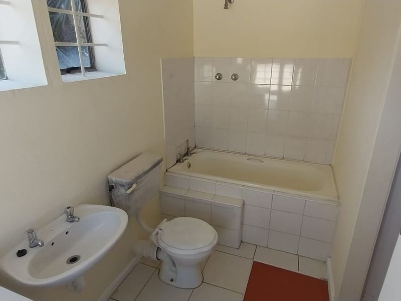 A functional bathroom featuring a bathtub, pedestal basin, and toilet, with tiled finishes and security bars on the windows.