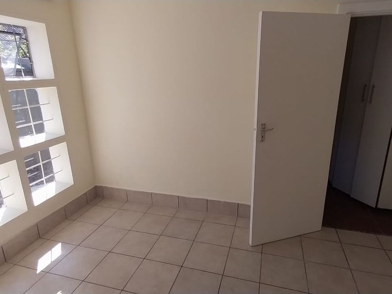 An empty bedroom featuring tiled flooring, built-in cupboards, and a distinctive grid-style window with security bars.