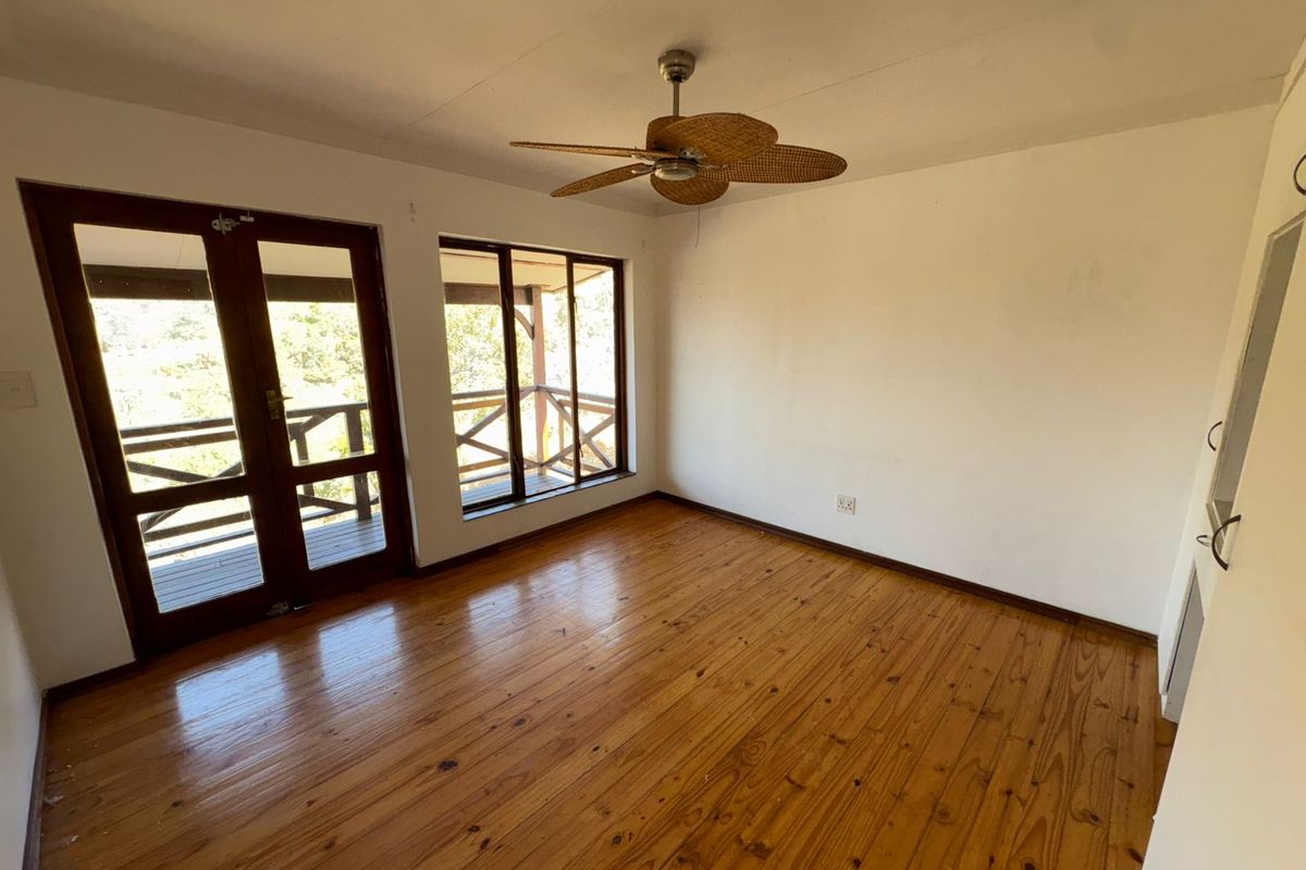 An empty bedroom featuring polished timber flooring, a ceiling fan, and direct access to an outdoor balcony through timber-framed glass doors.