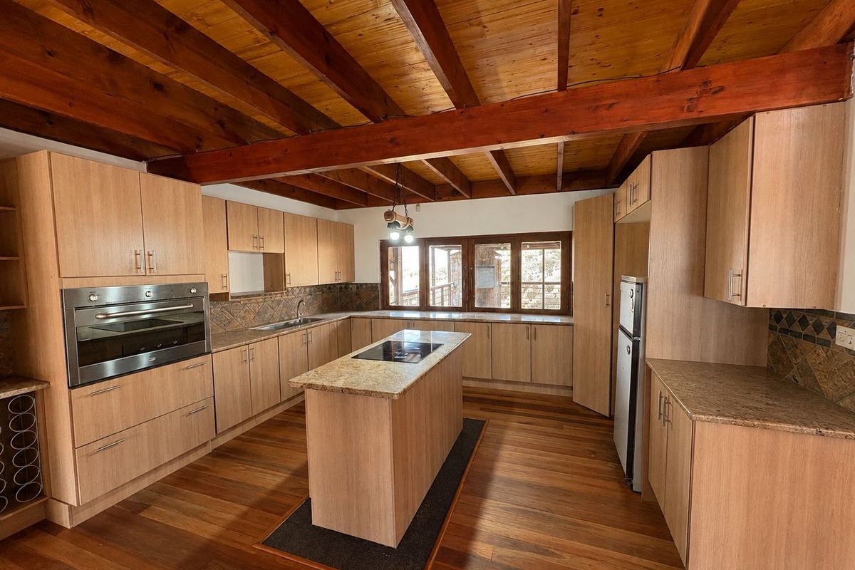 Spacious kitchen featuring warm timber flooring, exposed ceiling beams, stone countertops, a central island, and built-in appliances with ample cabinetry.