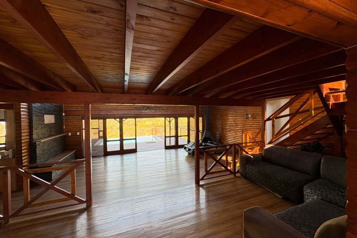 Spacious living area featuring exposed timber beams, warm wood paneling, a stone fireplace, and large stacking doors opening to the outdoor pool area.
